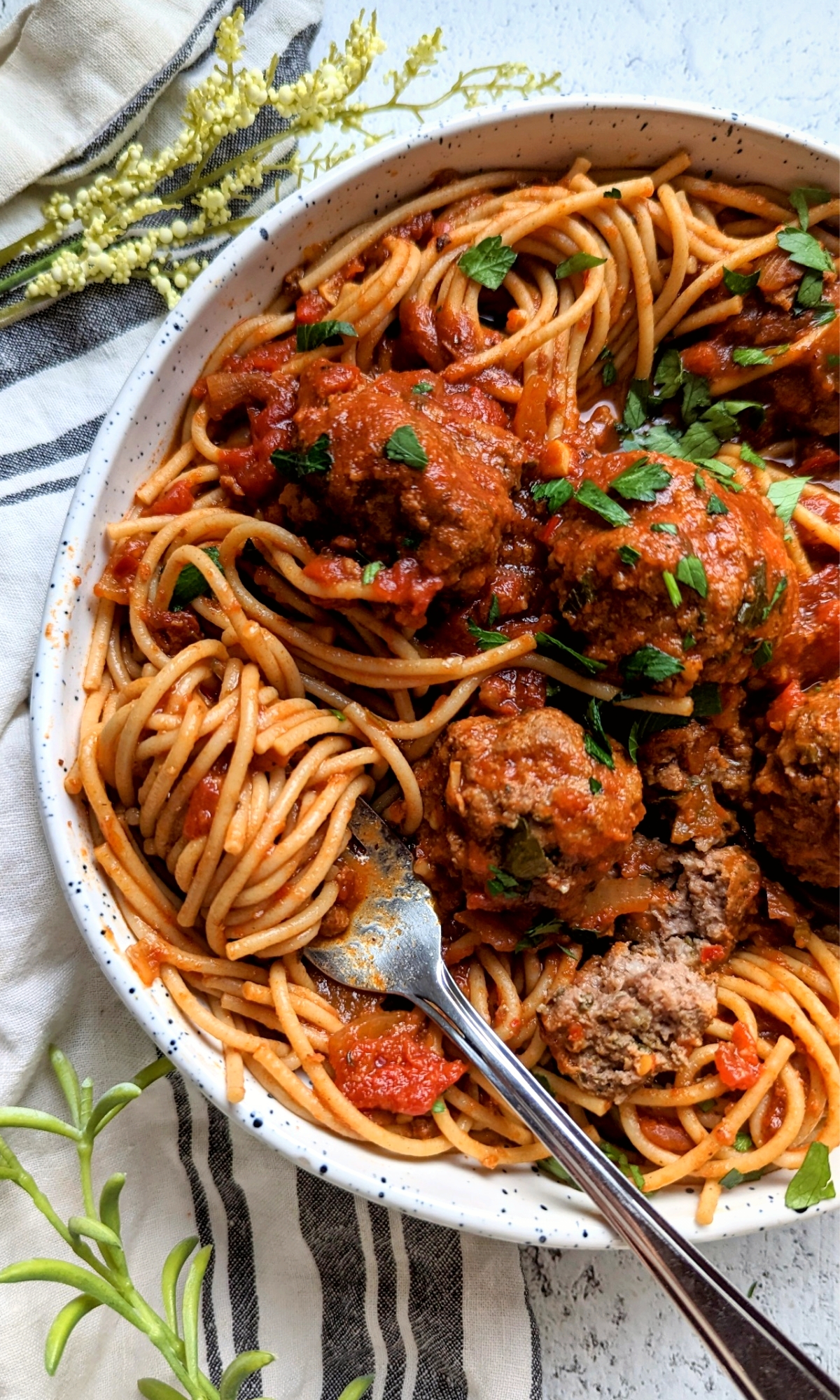 gluten free spaghetti and meatballs with tomato sauce and parsley in a beautiful bowl and fork twirl pasta.