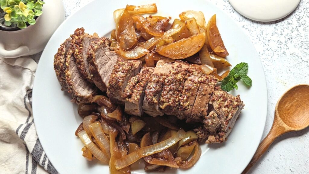 dutch oven baked pork tenderloin recipe on a plate with slow cooked onions and fresh apples with fresh herbs