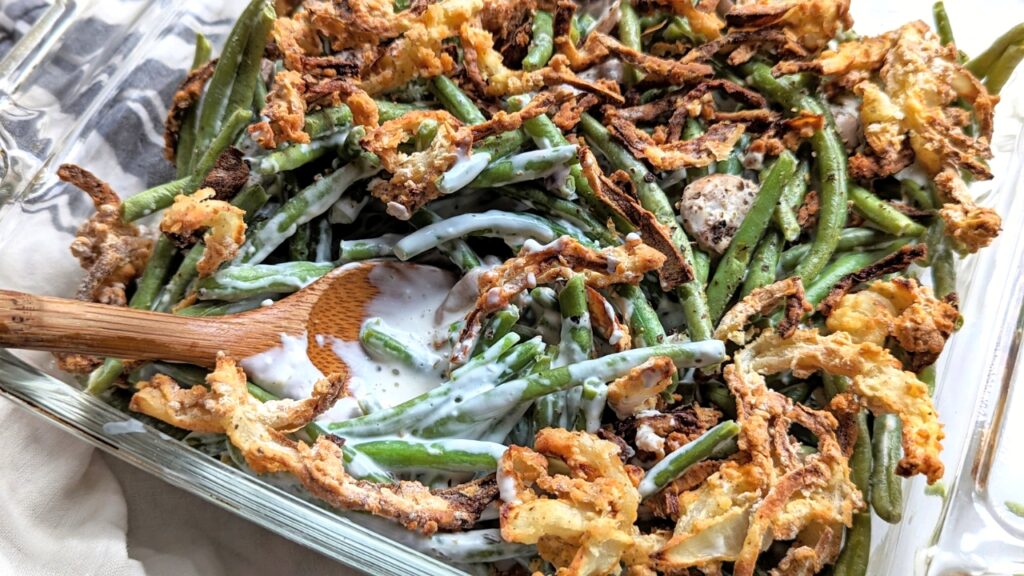 green bean cream cheese casserole recipe with crispy onions and fresh green beans in a baking dish with a wooden spoon.