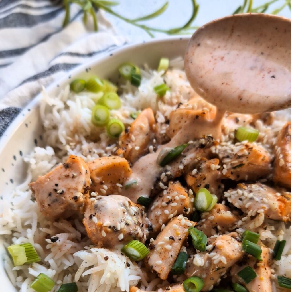 a bowl of crispy salmon topped with bang bang sauce over rice with green onions and scallions