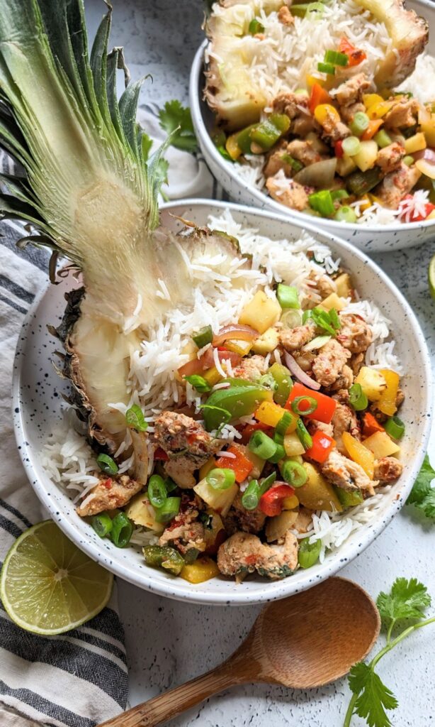 chicken served in a hollowed out pineapple bowl with white rice and red and green bell peppers