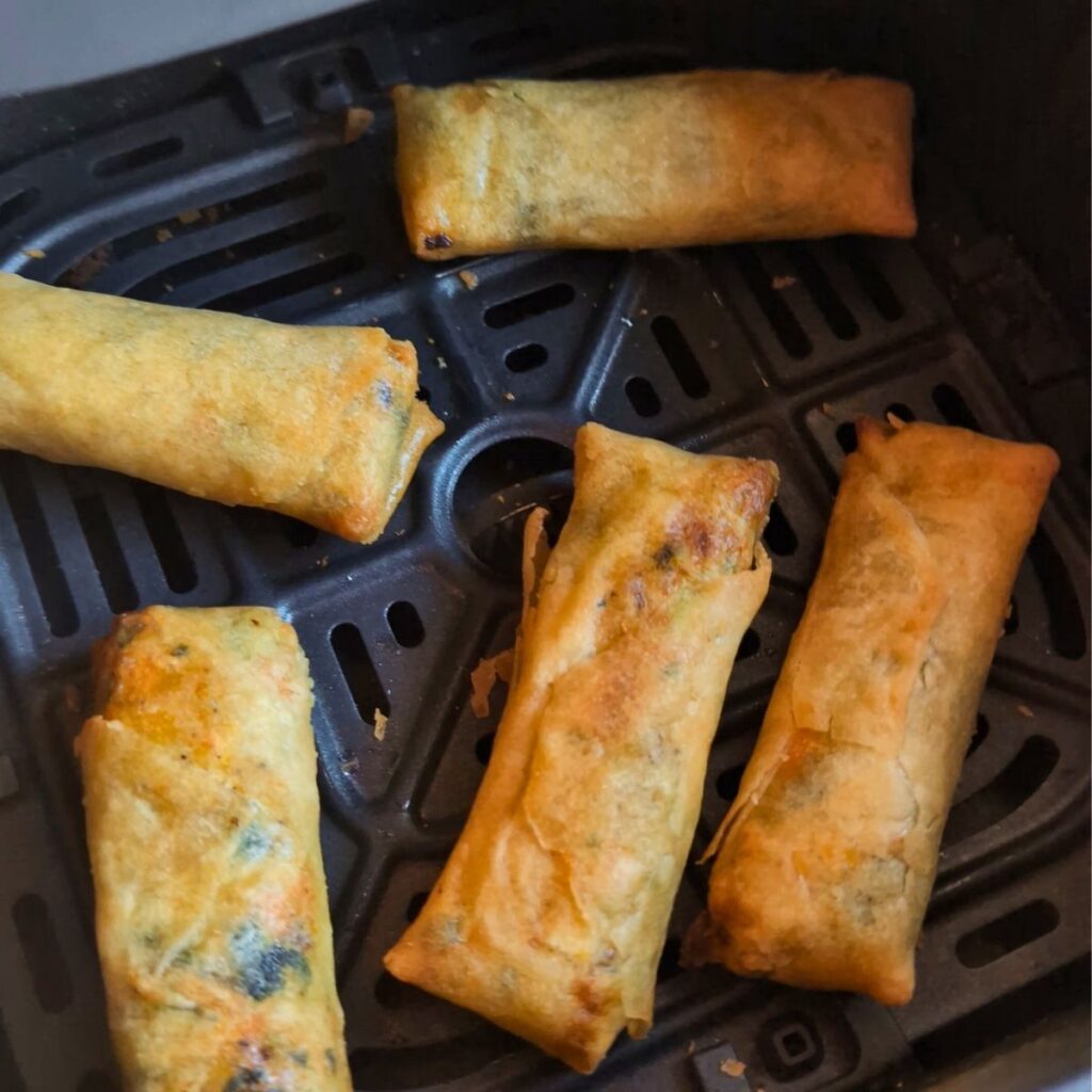 vegetable spring rolls in air fryer basket with a little cooking spray to make them light brown