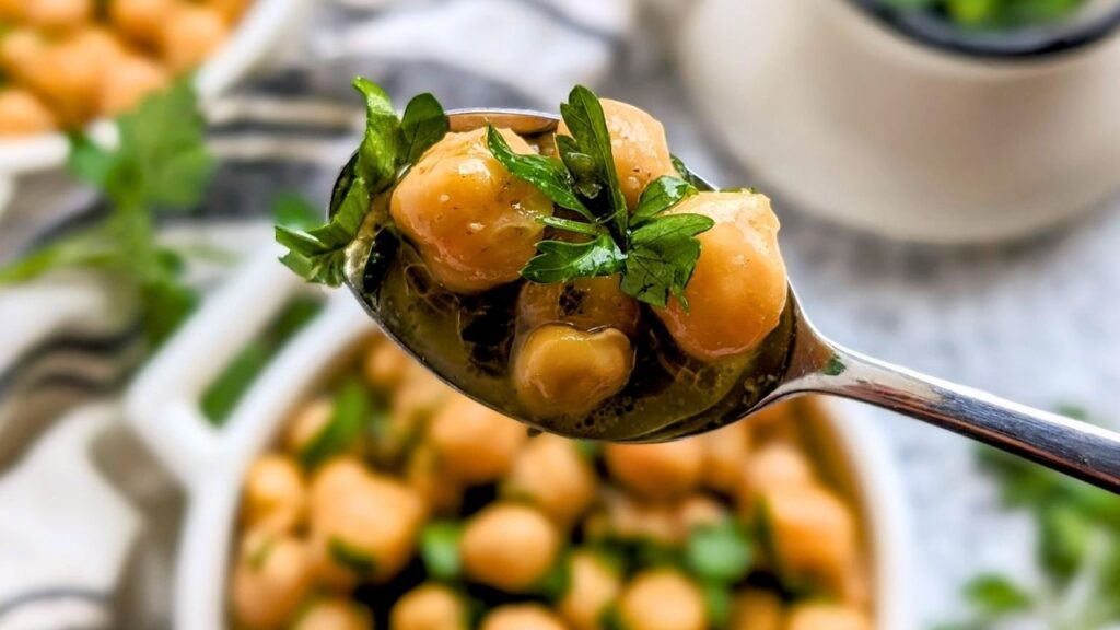 greek chickpeas recipe with parsley and cumin on a spoon with fresh herbs over a dish of chickpeas that are homemade
