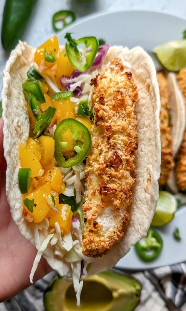 fish tacos with mango salsa with jalapeno peppers and green cabbage on a flour tortilla