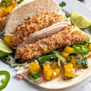 white fish fillets in corn tortilla taco shells with spicy mango salsa and peppers on a plate