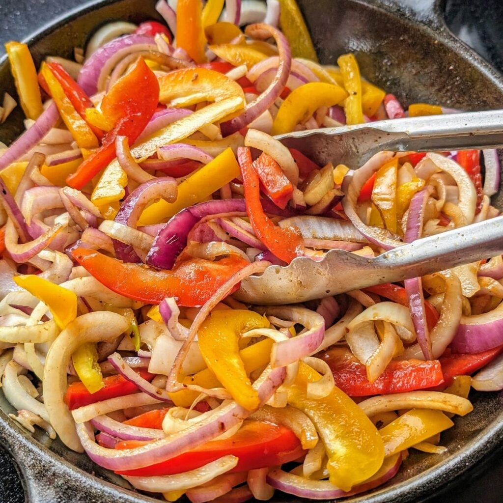 fajita vegetables cooking in a cast iron skillet red onions bell peppers and red pepper