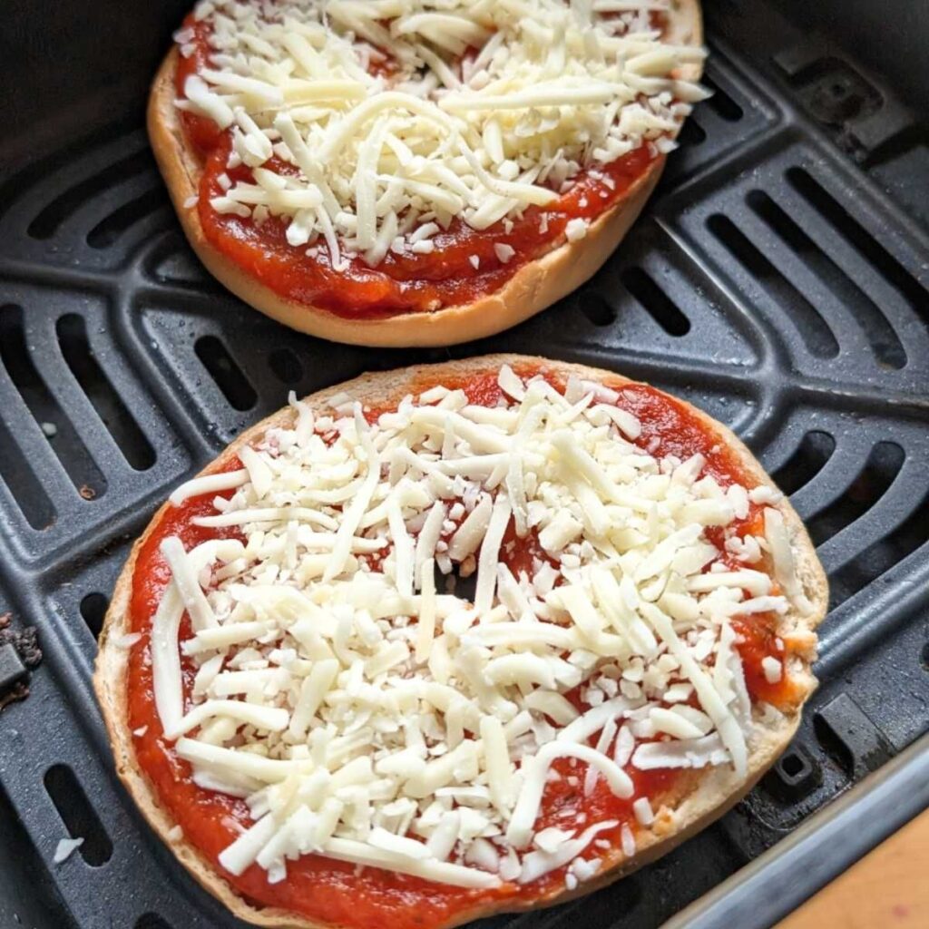 a plain bagel topped with pasta sauce and shredded mozzarella cheese in an air fryer basket about to get gooey