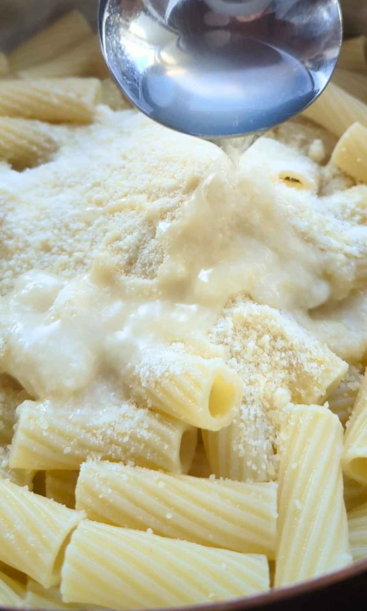 pasta cooking water and romato cheese being added to cooked pasta.