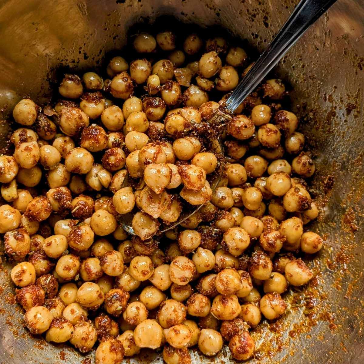 canned chickpeas in a bowl tossed with shawarma spices with a spoon.