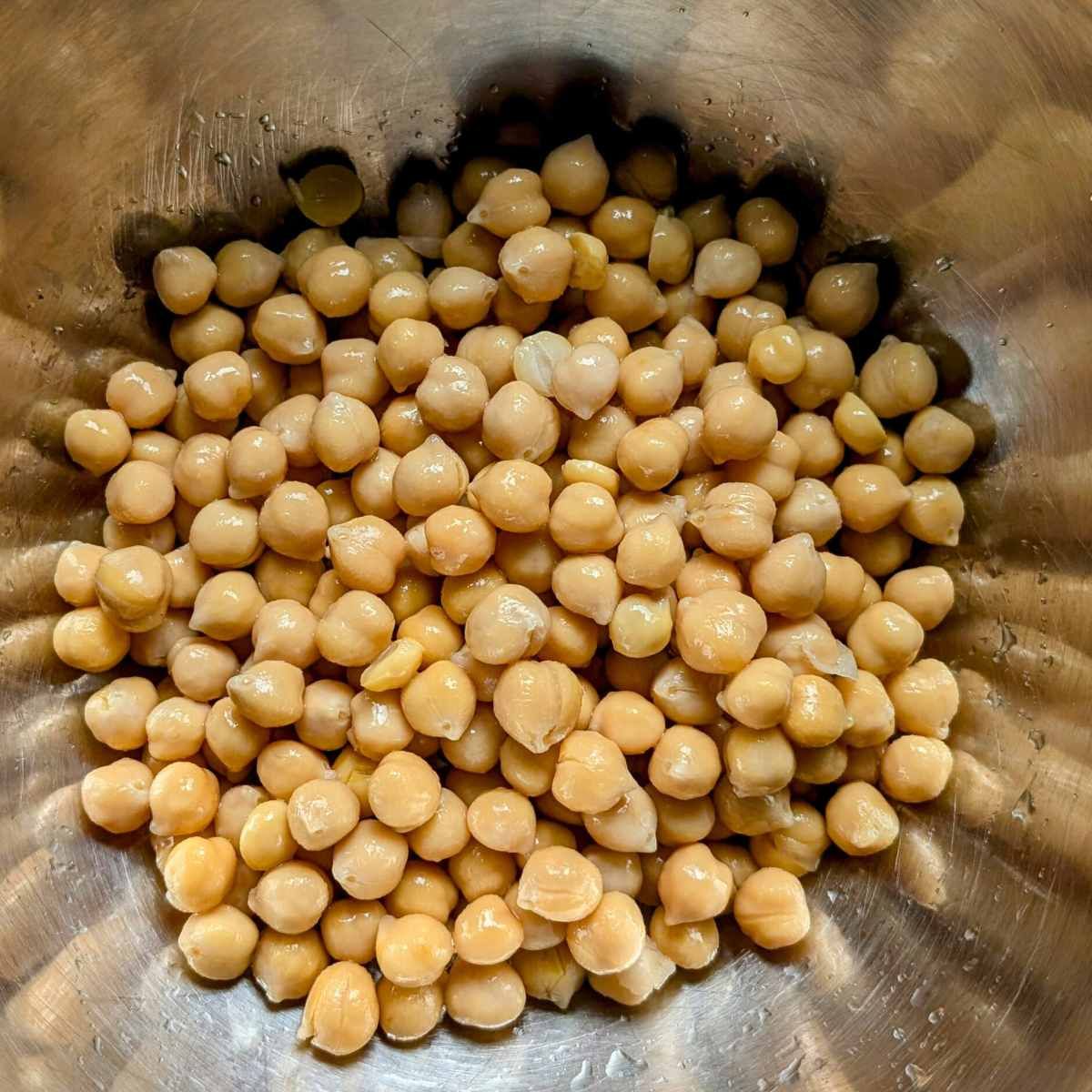 a can of chickpeas that have been drained, rinsed, and placed in a mixing bowl.