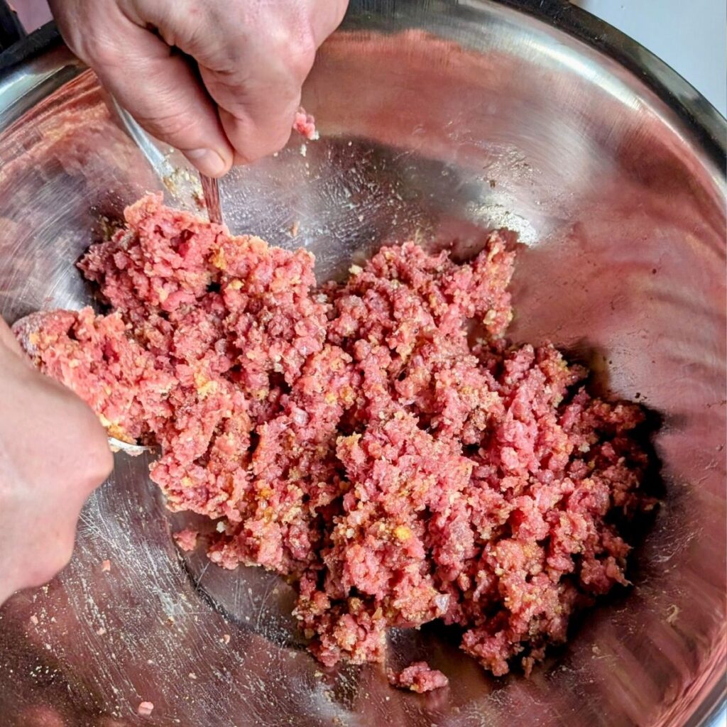 mixing ground brisket meat with spices and breadcrumbs with spoons.