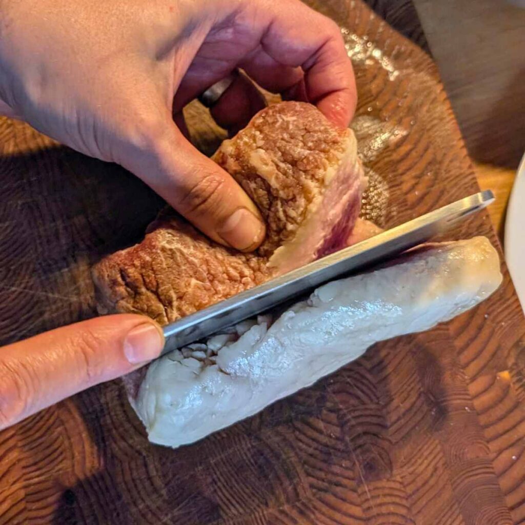 trimming fat off a brisket using a sharp japanese kitchen knife with folded steel.