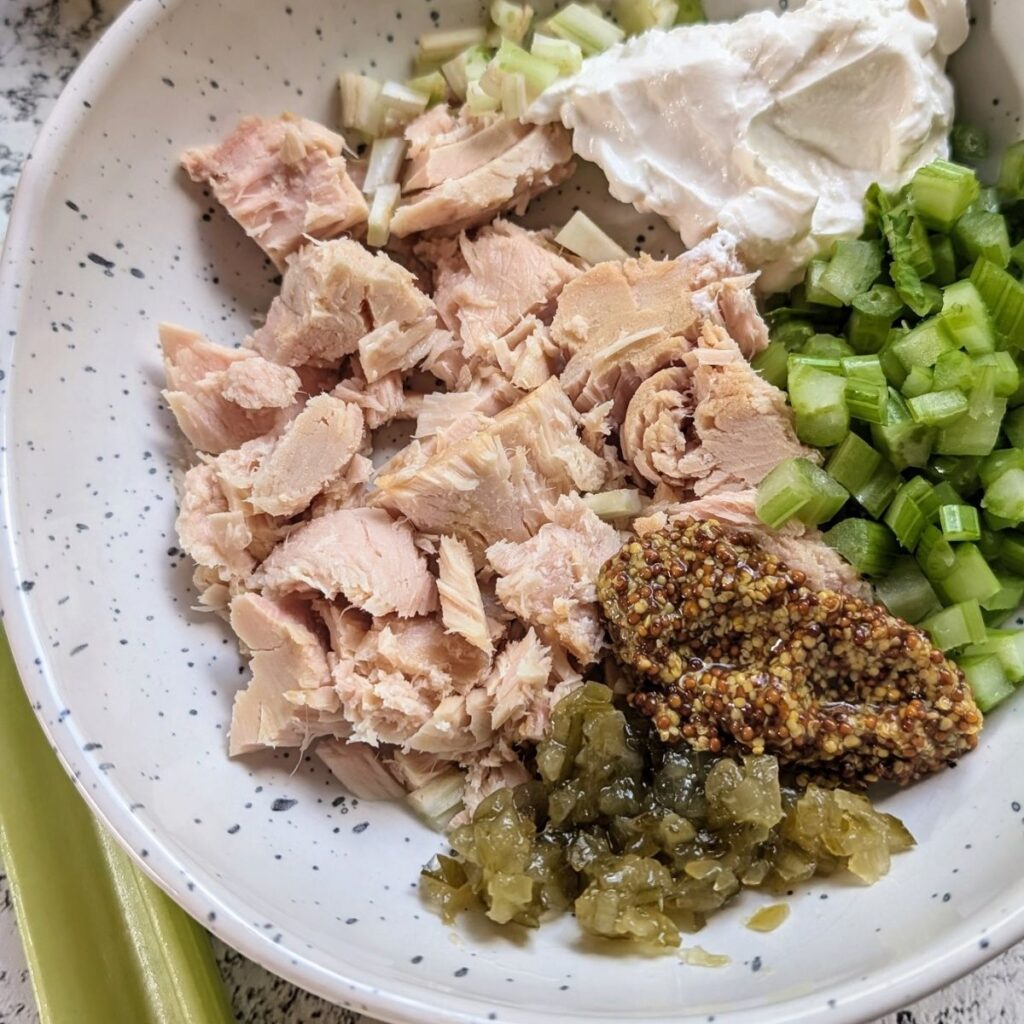 a mixing bowl with canned tuna, dijon mustard, celery, onion, relish, and greek yogurt.