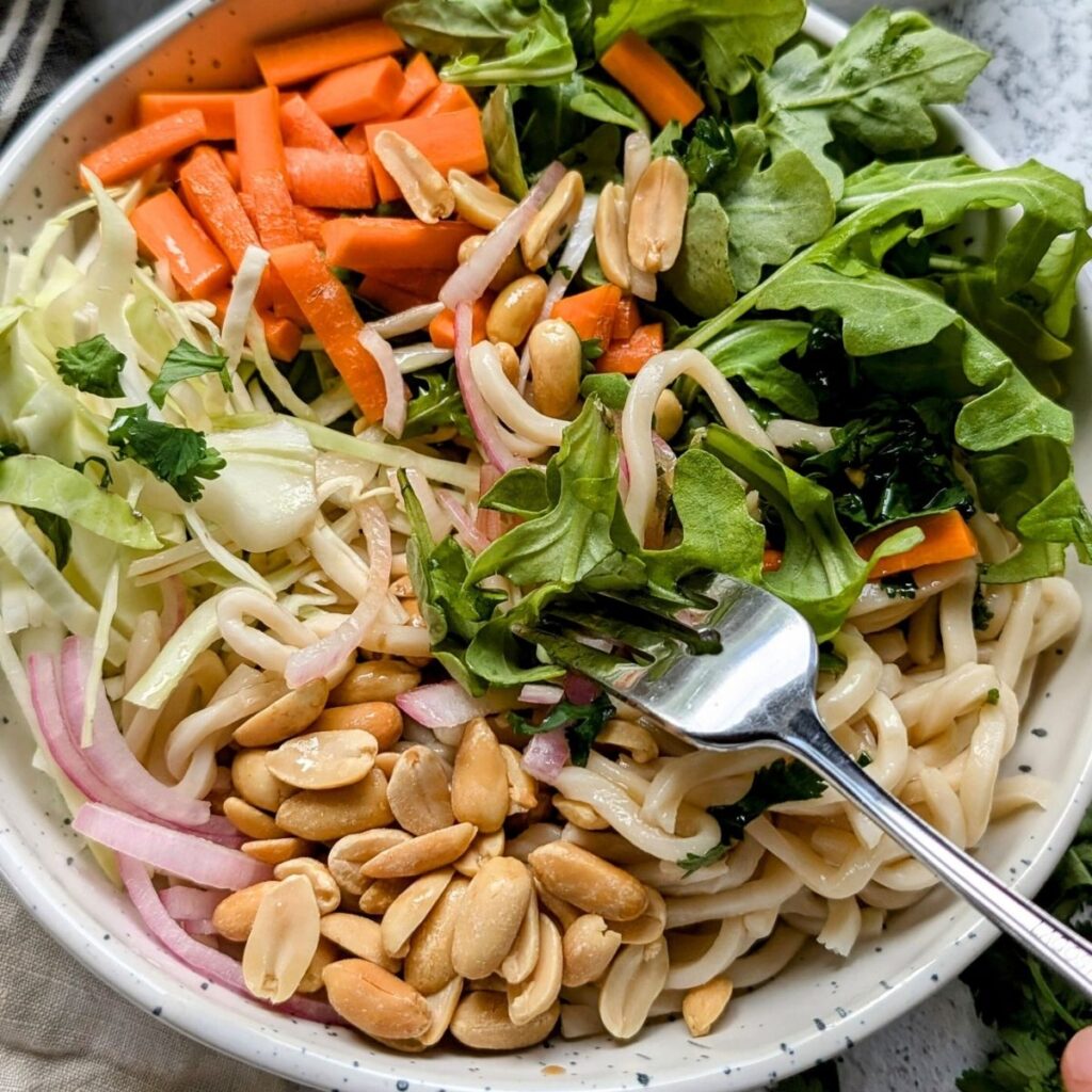 a fork tossing the thai noodle salad with sesame lime dressing well to combine the dressing and ingredients.