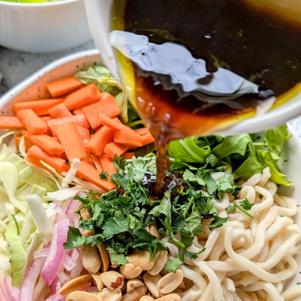 sesame lime dressing being poured over a thai wheat noodle salad from trader joe's noodles in a package.