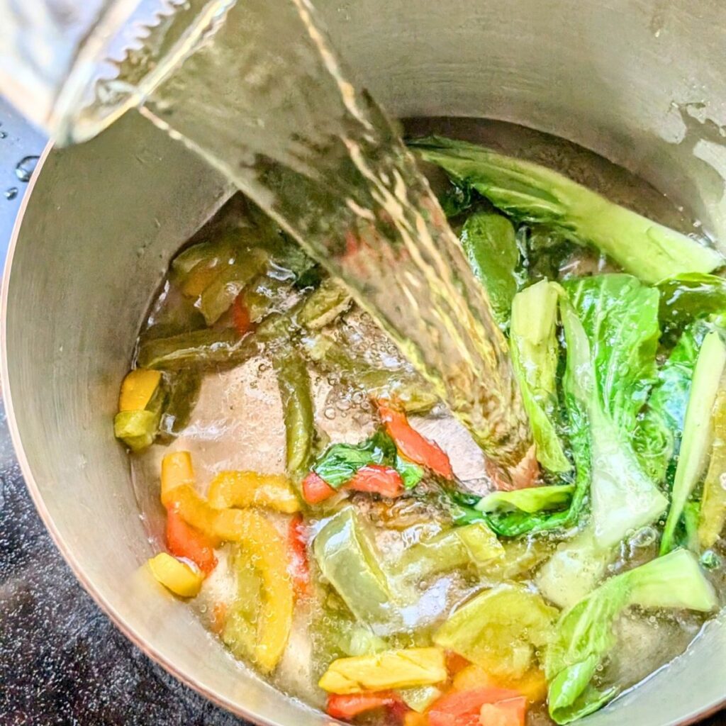 Vegetable stock being added to a pot with sauteed asian vegetables to make thai soup.