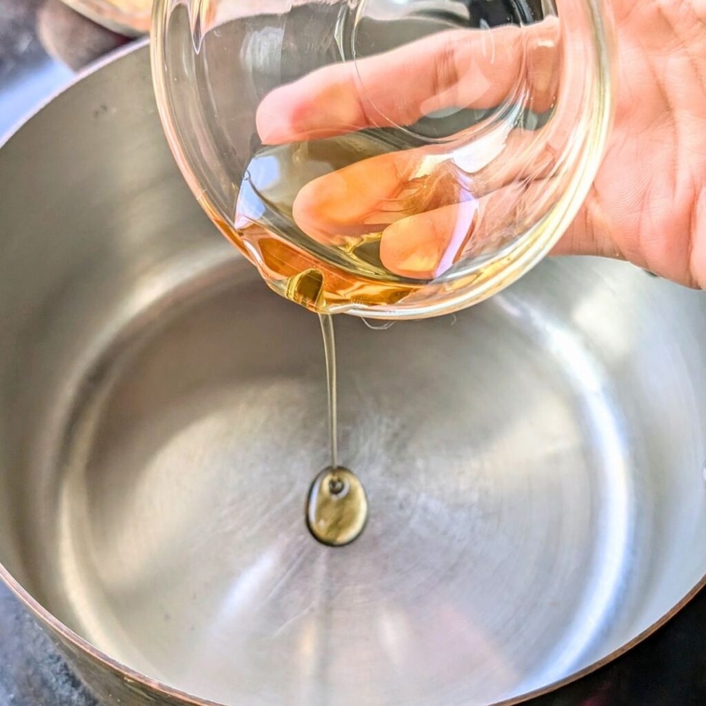 sesame oil being heated in a small soup pot being poured from a ramekin.