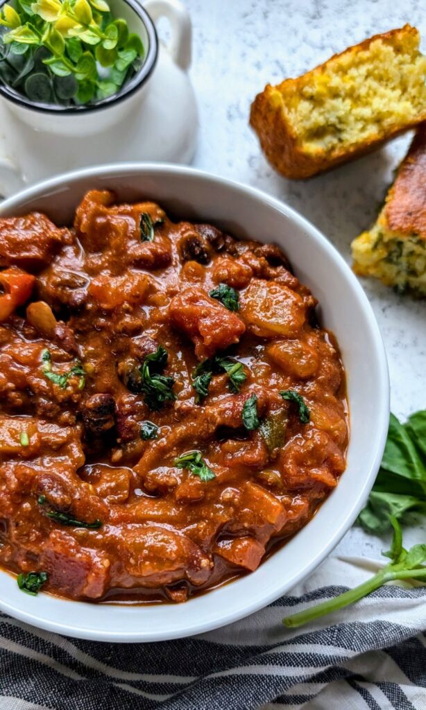 a bowl of bison chili with cornbread topped with fresh cilantro, filled with beans, tomatoes, and chili spices.