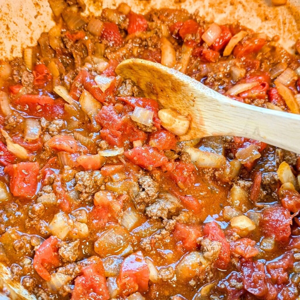 a large pot of buffalo chili with tomatoes and spices stirred with a wooden spoon.