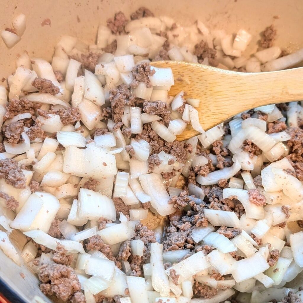 a dutch oven with ground bison meat and onions and garlic browning in a pot cooking for chili.