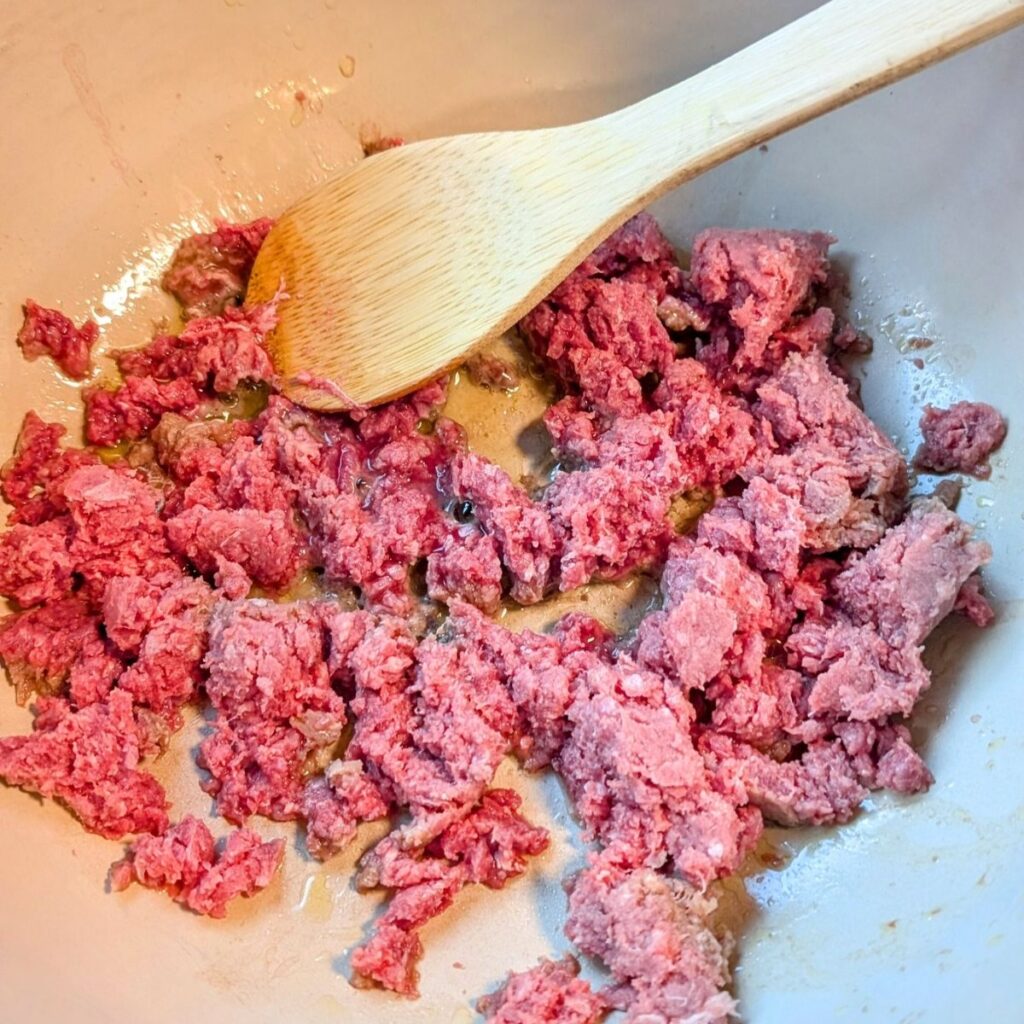 browned bison meat in a pot being stirred with a spoon to cook it in a dutch oven.