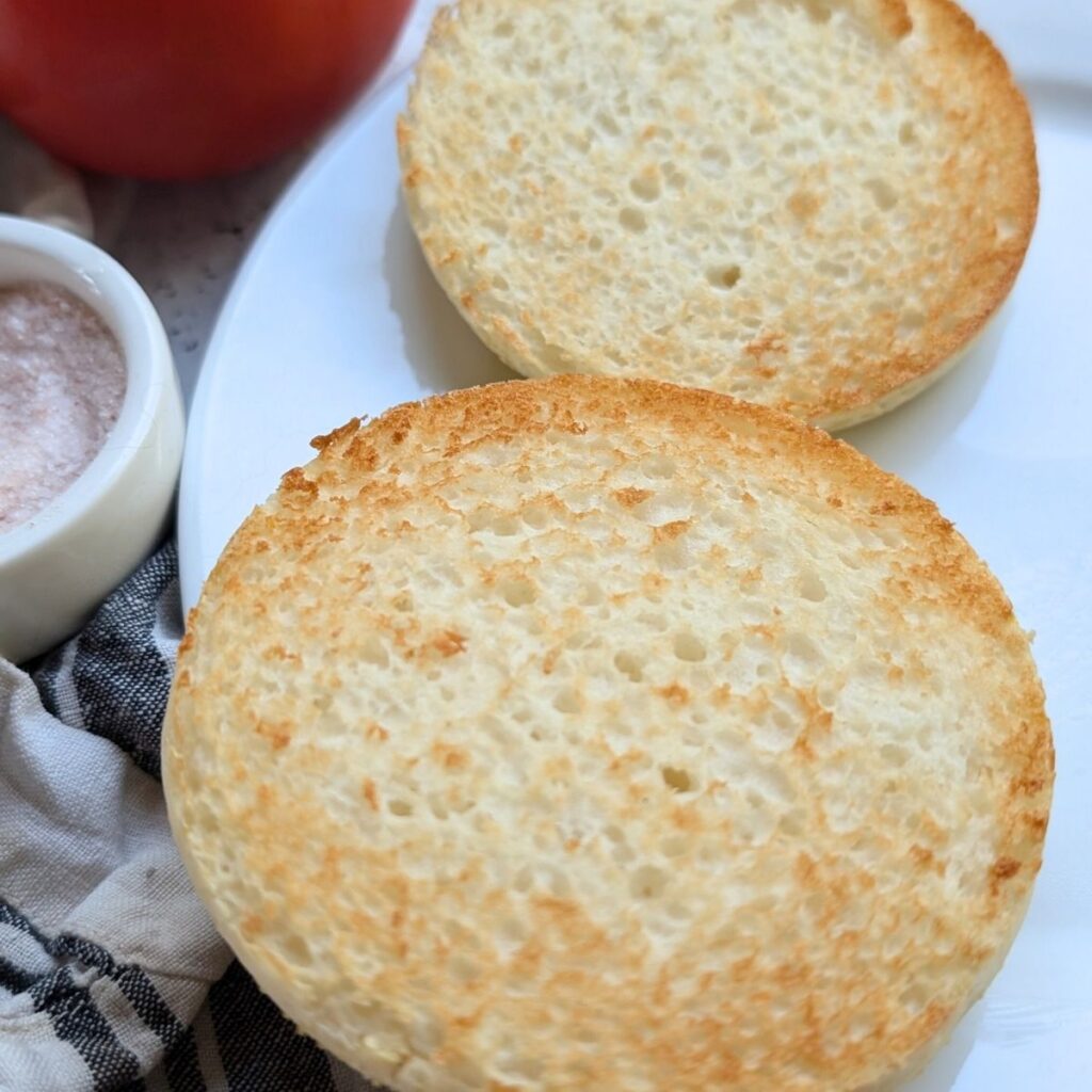 toasted gluten free english muffins on a plate for a breakfast sandwich with caprese style fillings.