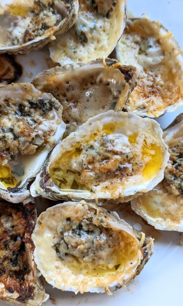 cheesy baked oysters on a plate with parmesan cheese and fresh parsley