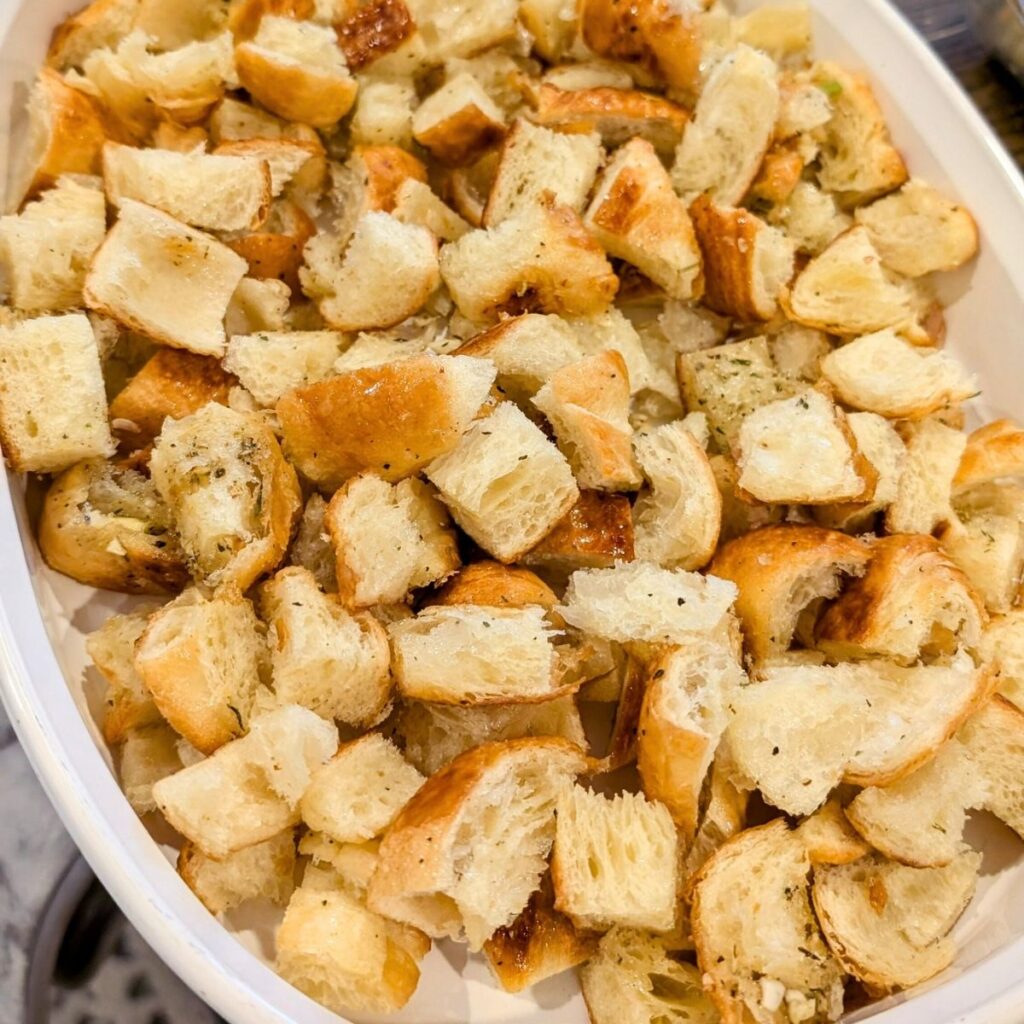 cubed bread in a baking dish covered with herbs and spices with garlic.