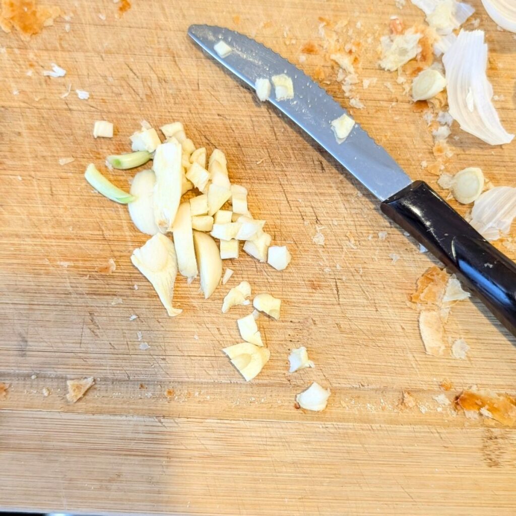 finely minced garlic on a cutting board with a steak knife.