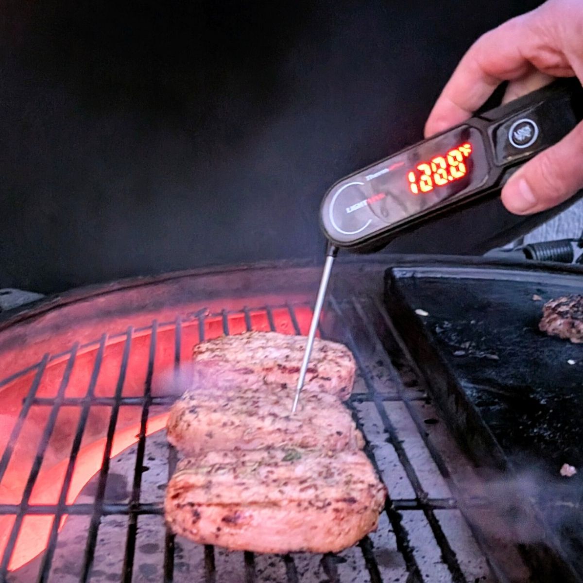 a meat thermometer checking a grilled pork chop on the big green egg