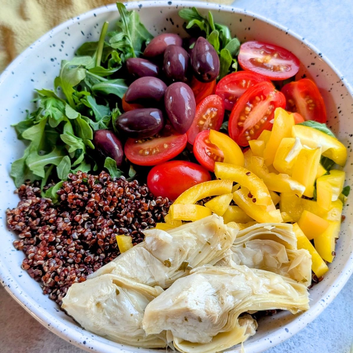 a red quinoa salad with bell peppers, olives, artichokes, and cherry tomatoes in a bowl.