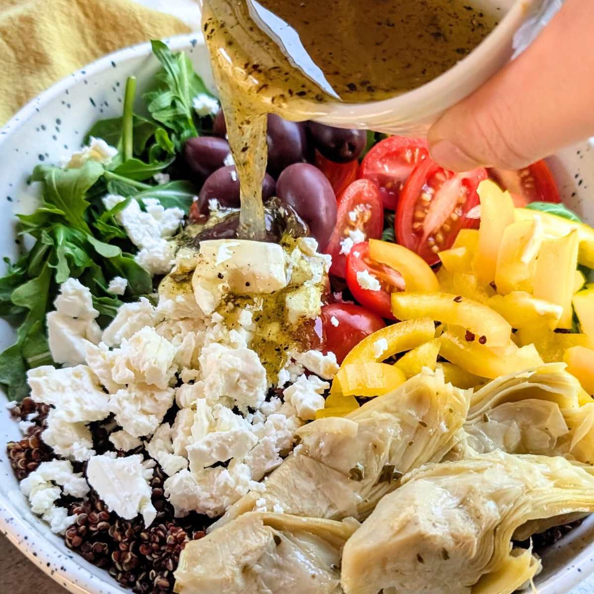 a lemon vinaigrette dressing poured over a feta quinoa salad with vegetables.