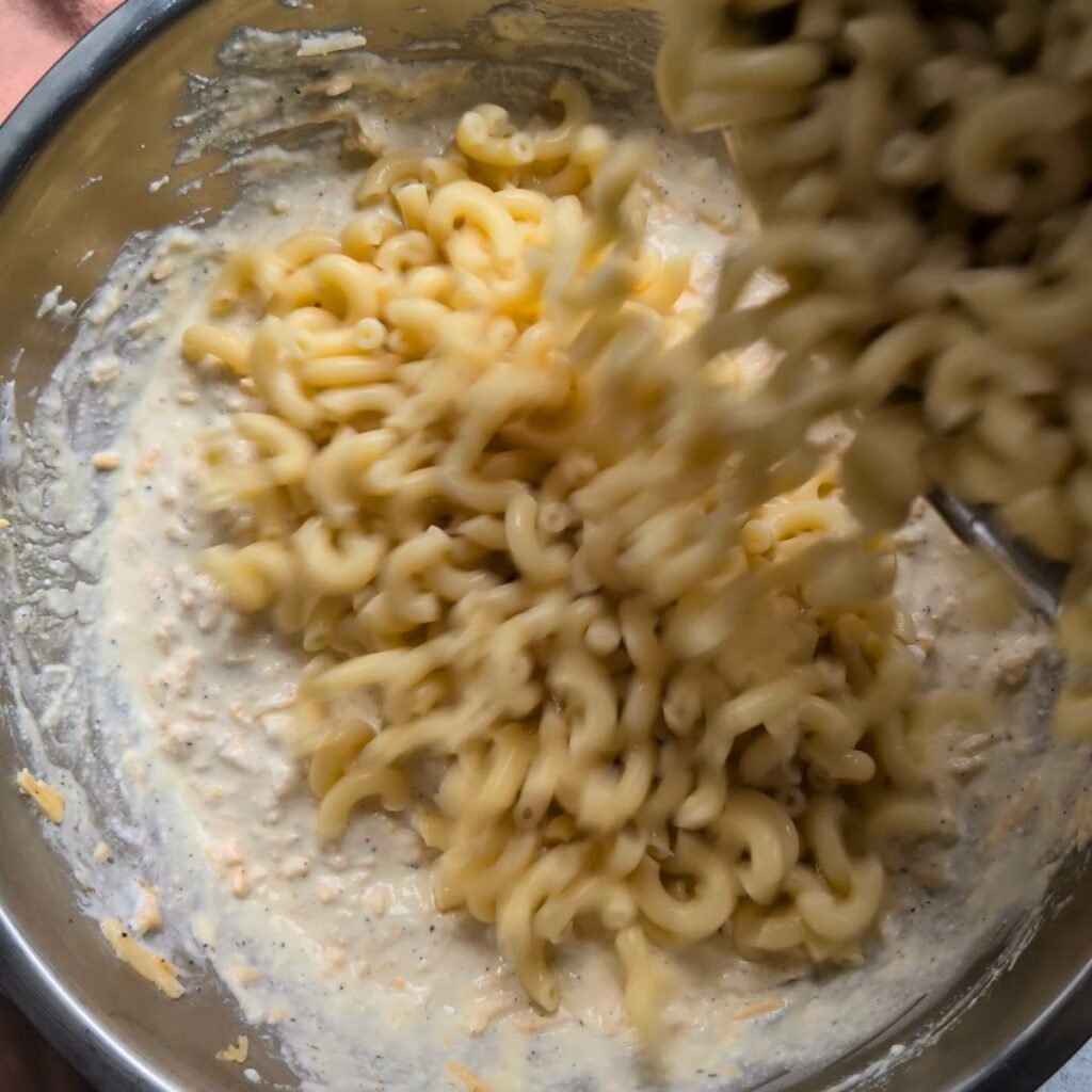 cooked macaroni noodles poured into a mixing bowl of ricotta and cheddar cheese to make mac and cheese.