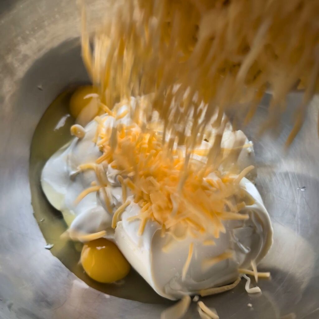 a mixing bowl with ricotta cheese, cheddar, sour cream, eggs, and salt and pepper for mac and cheese sauce.