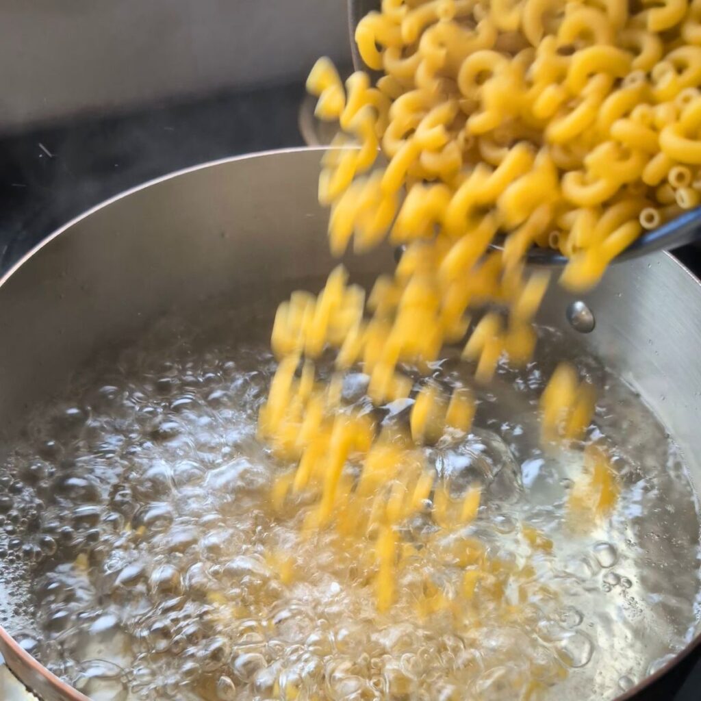 cooked macaroni noodles being added to a pot of boiling water for mac and cheese with ricotta