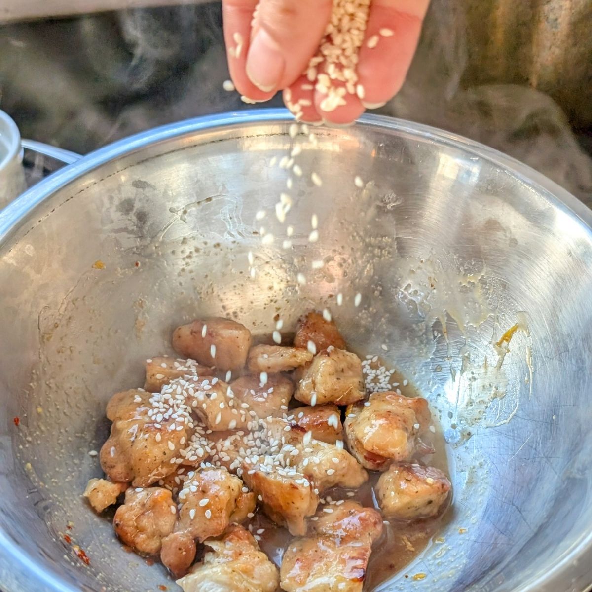 a hand sprinkling sesame seeds in a large mixing bowl with marmalade chicken