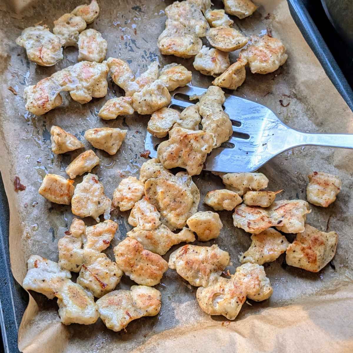 crispy baked chicken bites in the oven being flipped with a spatula to make orange marmalade chicken