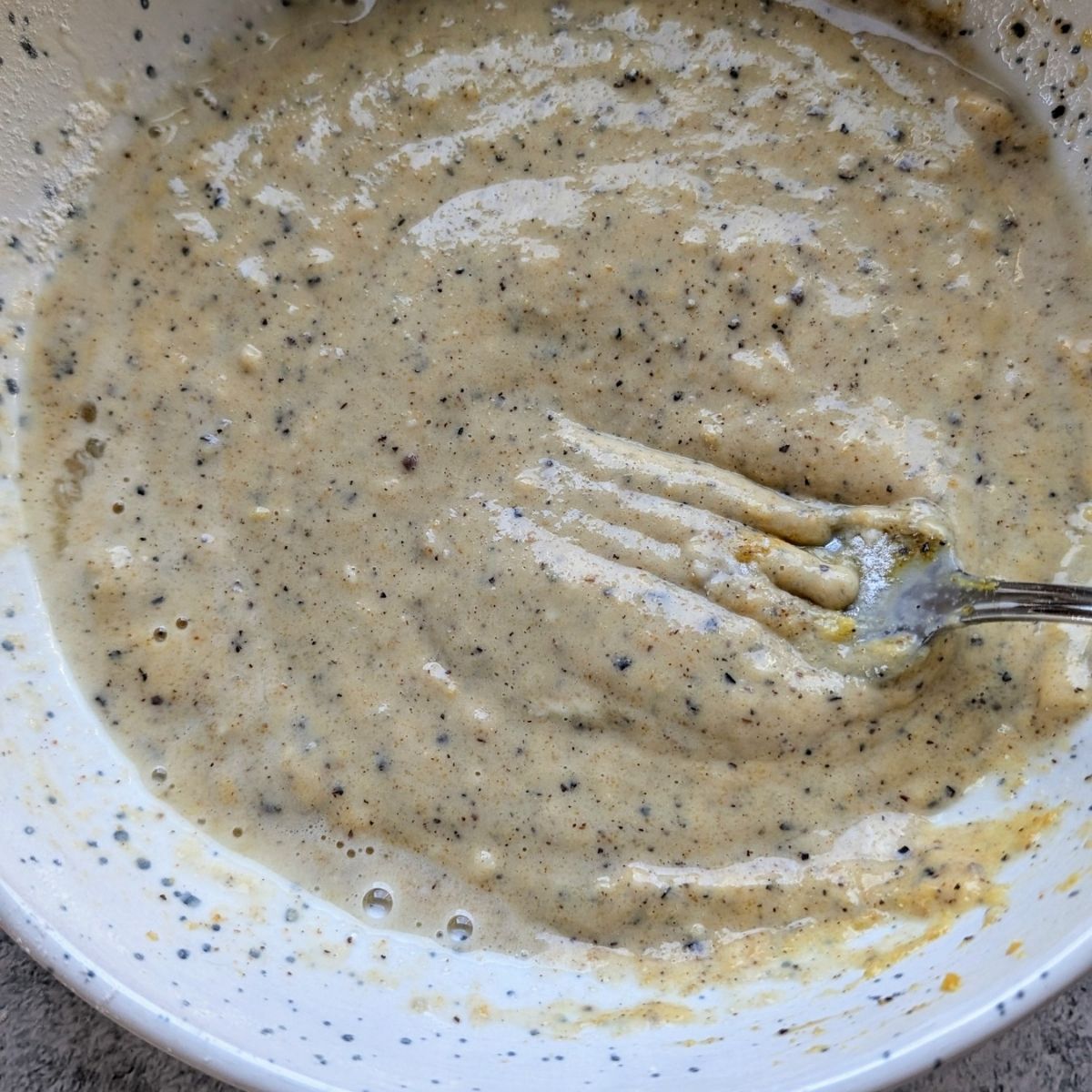 a fork mixing batter for orange chicken with eggs, black pepper, salt, flour, and garlic powder.