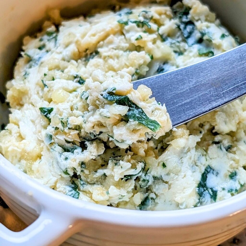 a butter knife spreading a pad of fresh garlic compound butter with parmesan cheese and parsley and chives.