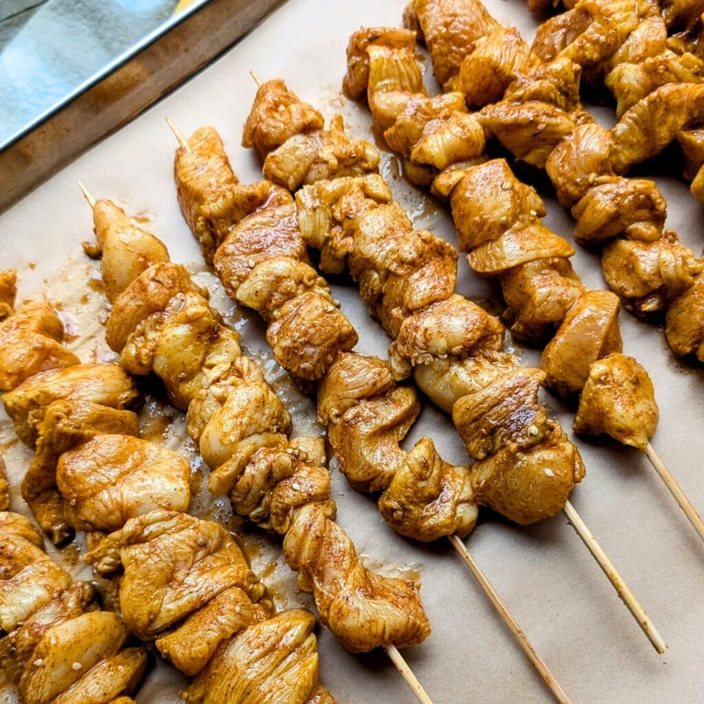 a baking sheet lined with parchment paper and rows of chicken shawarma skewers in the oven