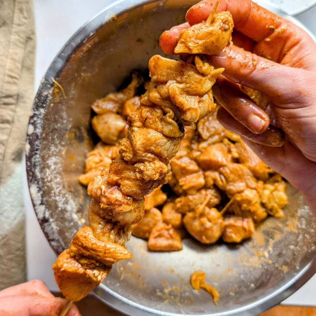 hands skewering chicken shawarma meat on a kebab to bake in the oven.