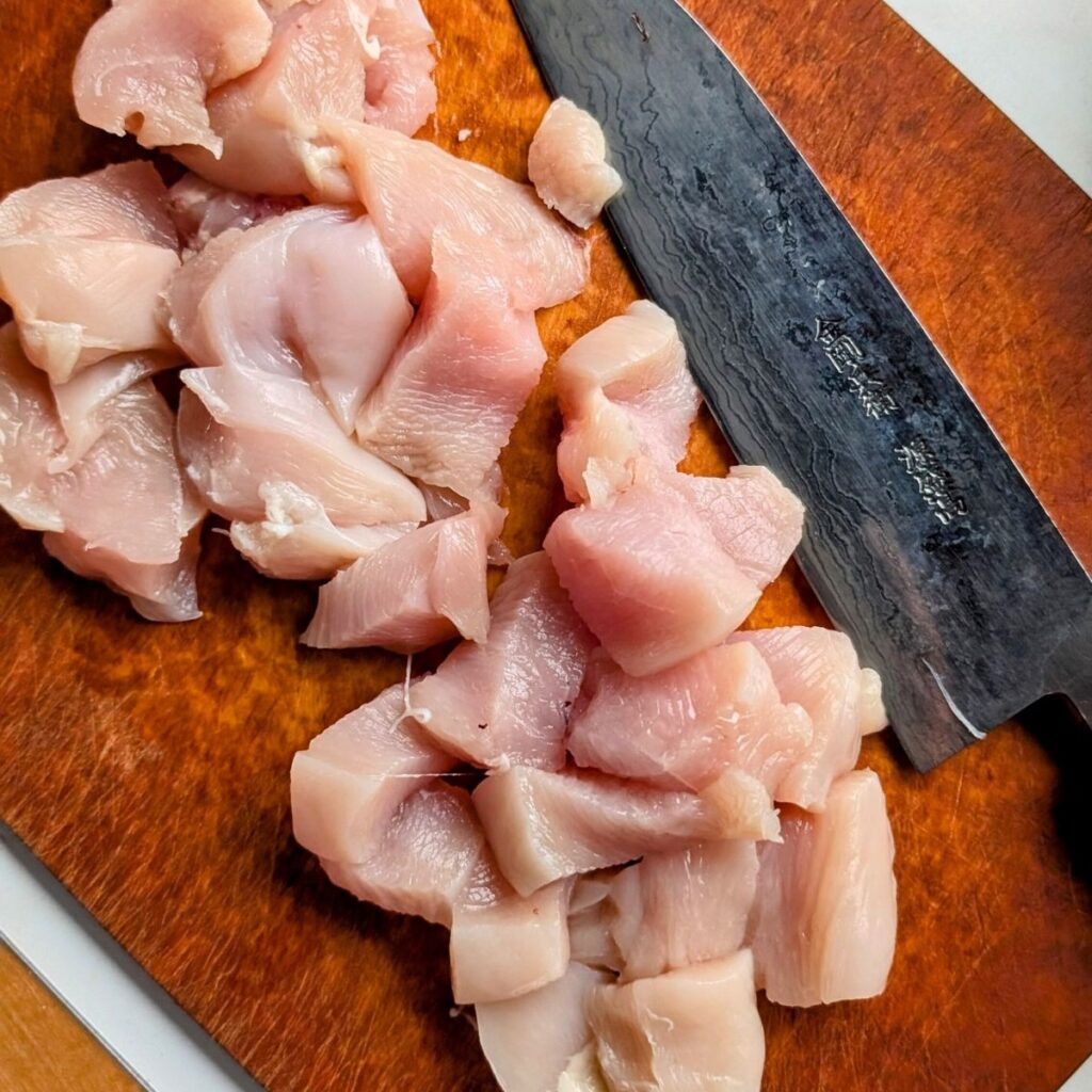 lean chicken breast meat on a cutting board cut into cubes to skewer