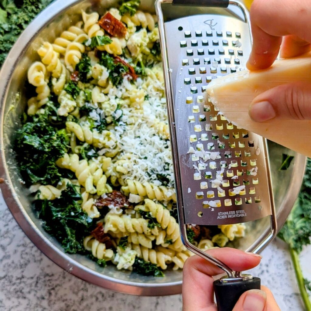 a hand grating fresh parmesan cheese over kale pasta salad from sam's club copycat recipe