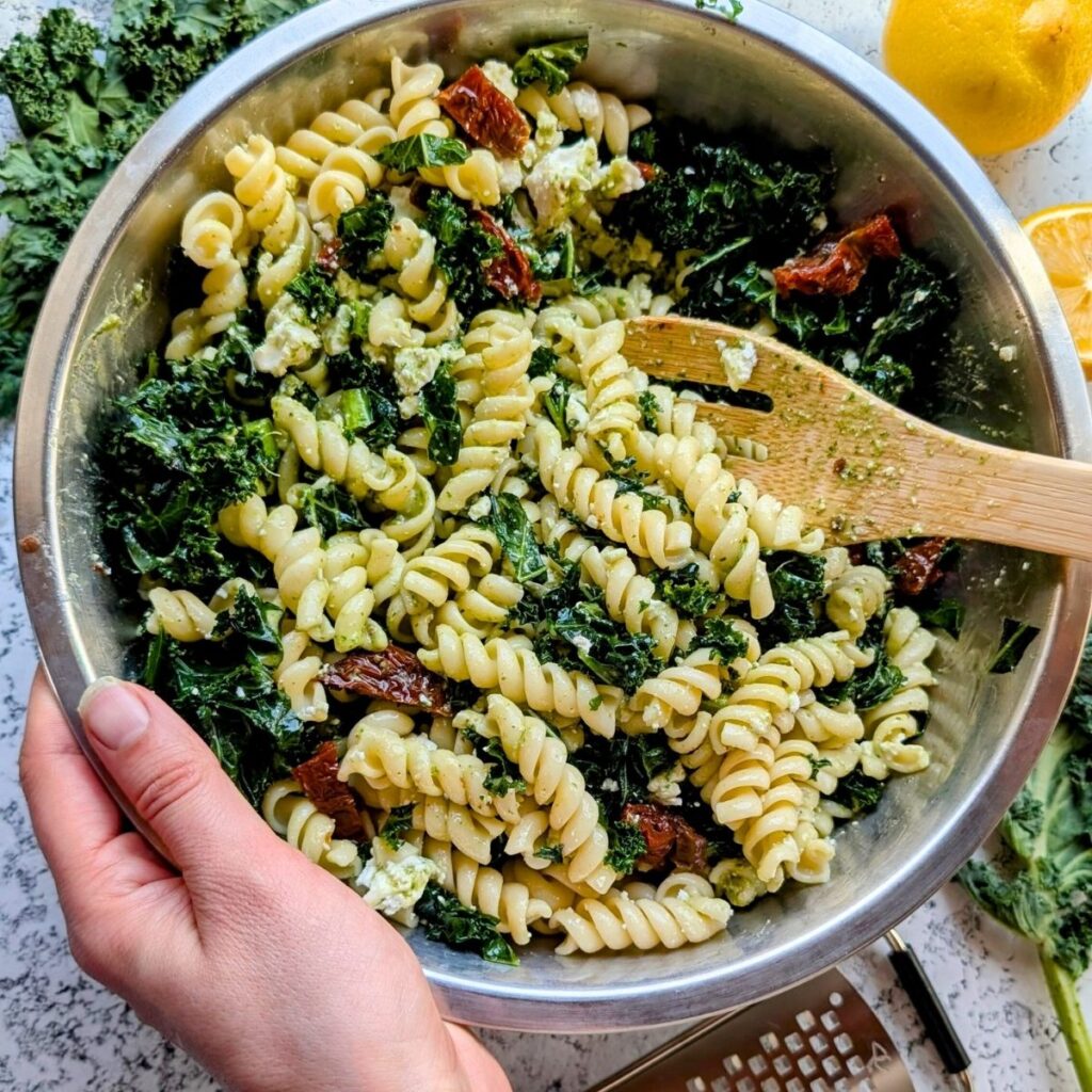 hands tossing copycat kale pasta salad with a wooden spoon for entertaining sam's club copycat recipes