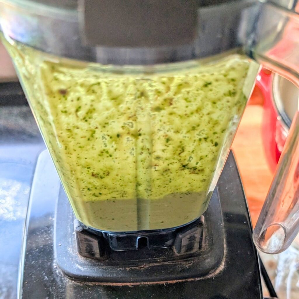 a blender full of green basil garlic oil dressing for Mediterranean pasta salad