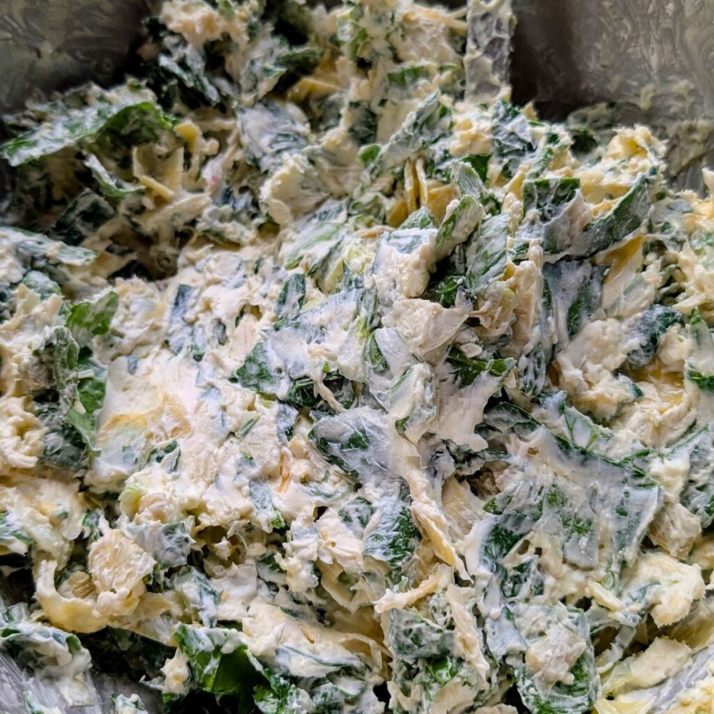 a big bowl of mixed spinach, artichoke hearts, cream cheese, parmesan cheese, and spices to make a dip.