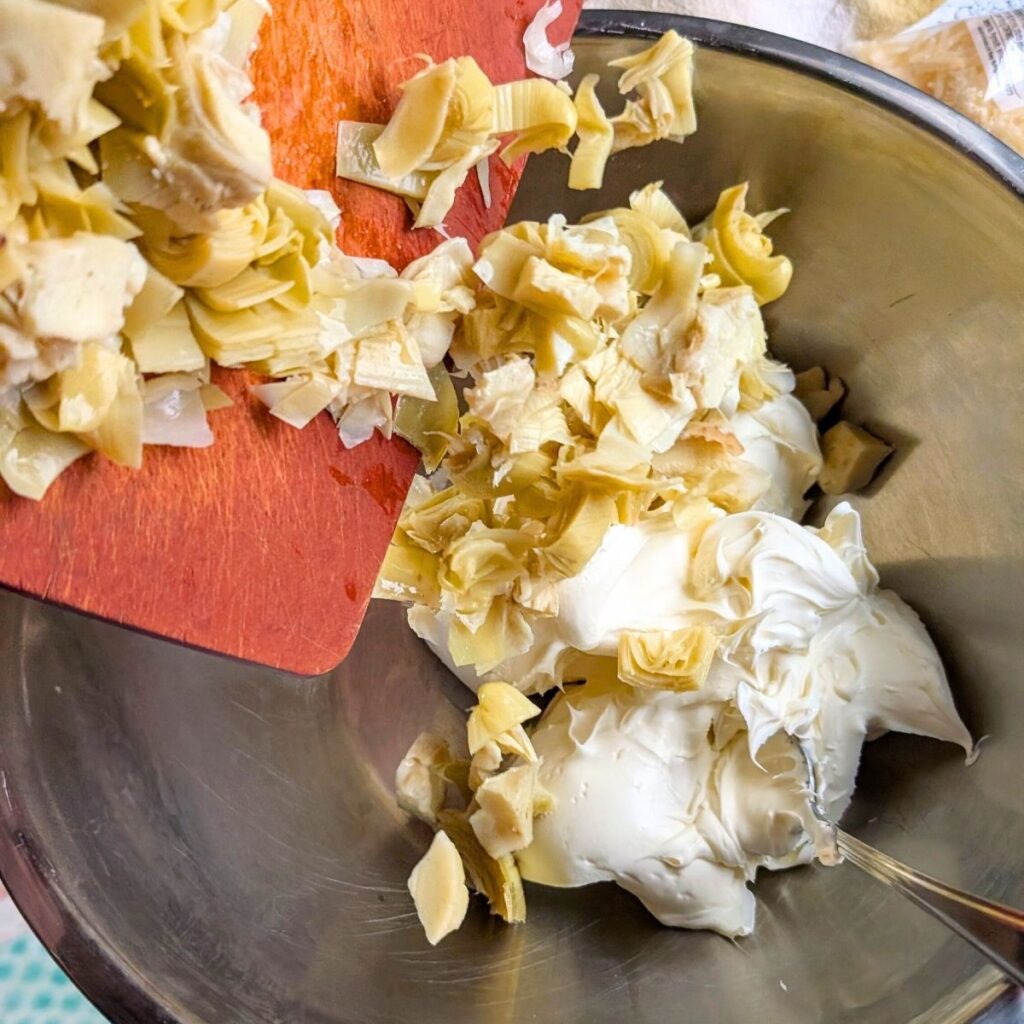 a large mixing bowl with cream cheese, chopped artichoke hearts, and other vegetables to make olive garden copycat dip.