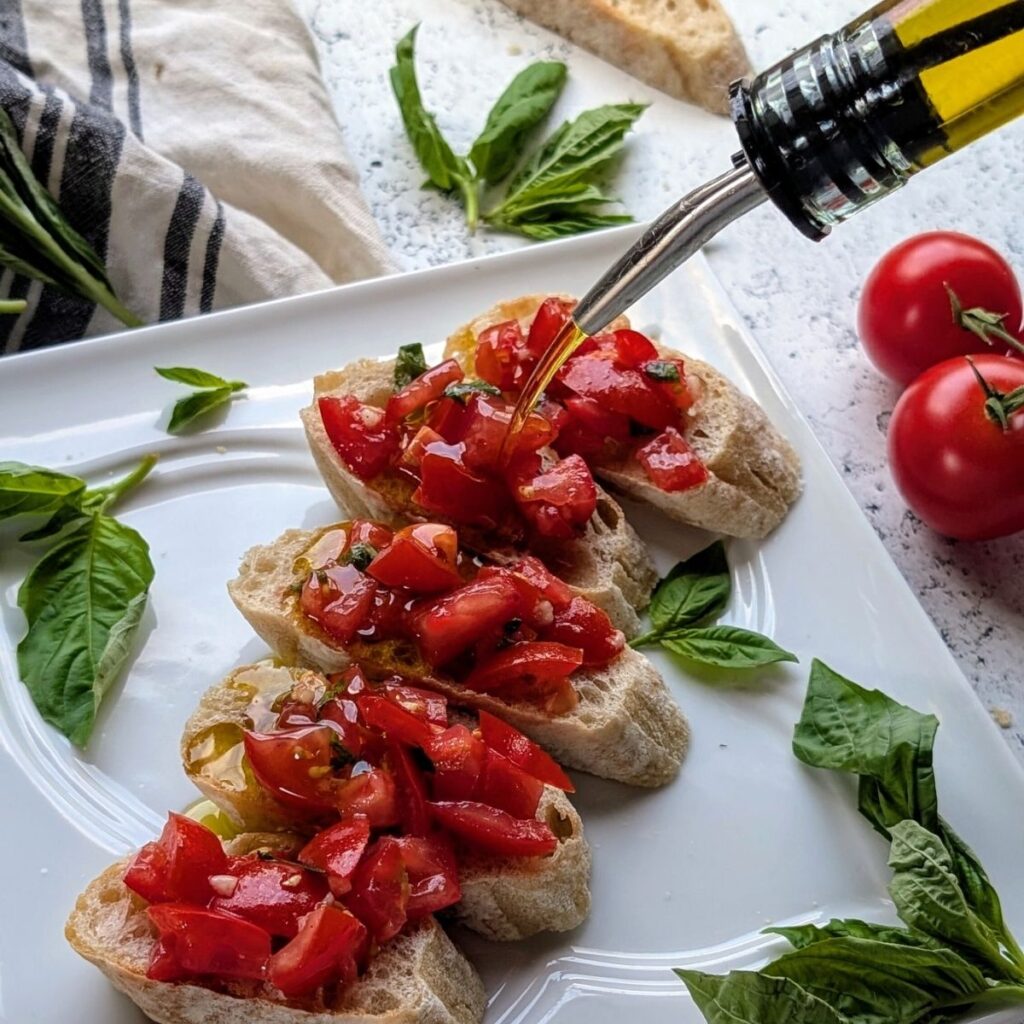 olive oil poured over bruschetta with olive oil drizzle and fresh basil on a plate.