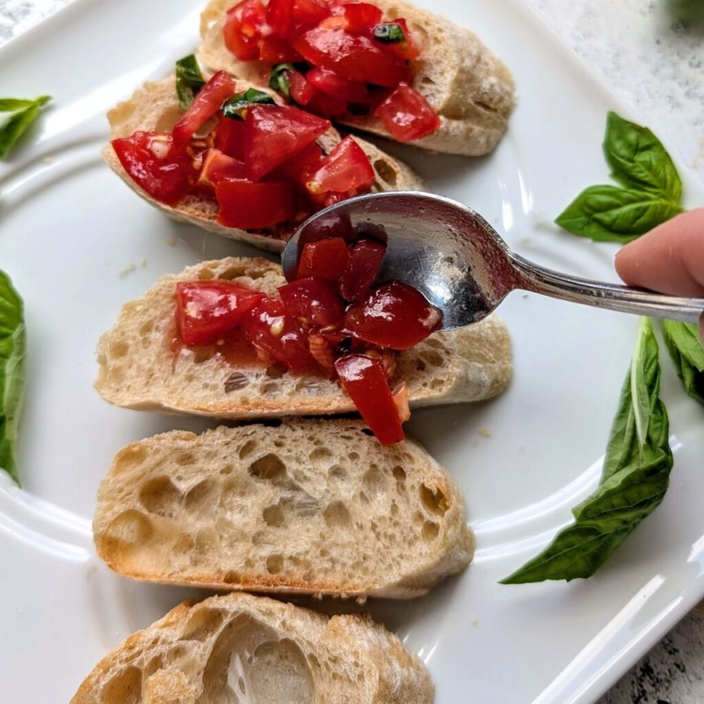 diced tomatoes over toasted  bread being spooned for a tasty summer appetizer.