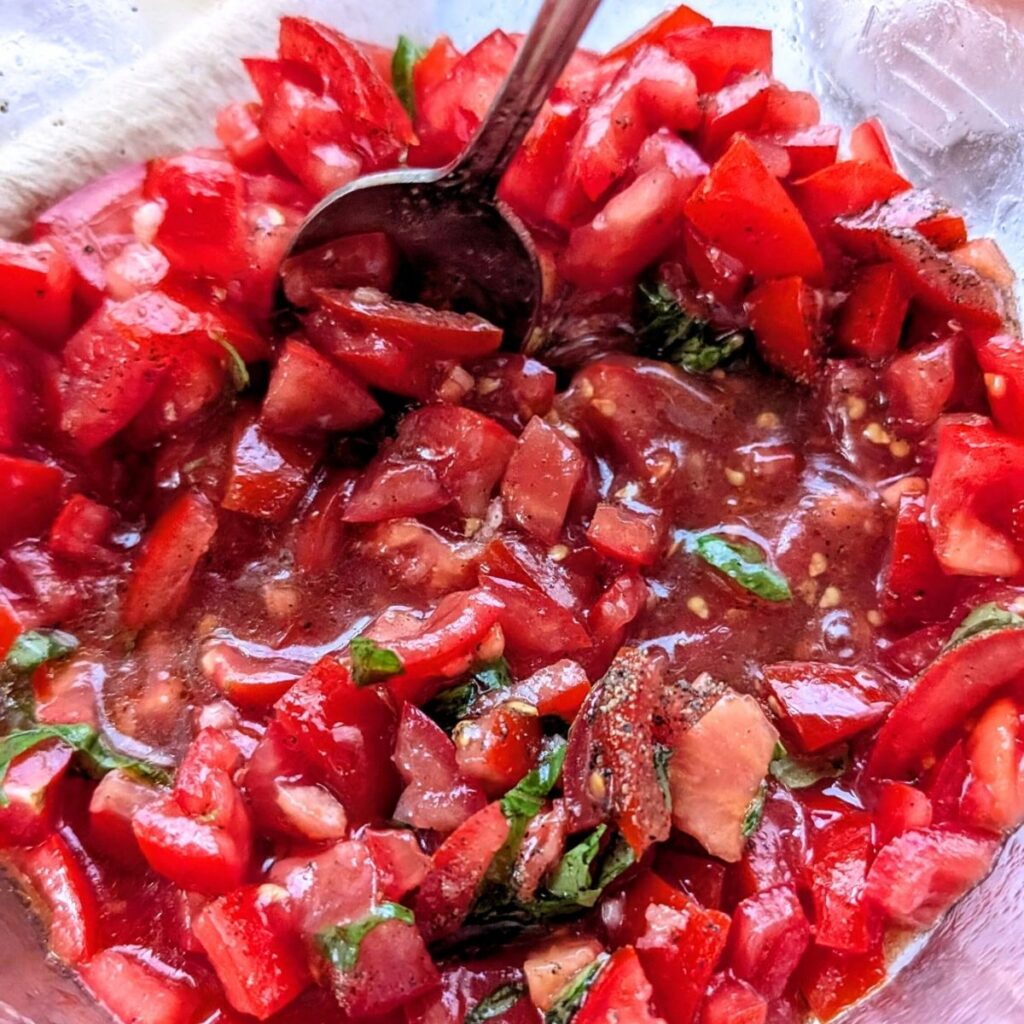 a spoon mixing copycat bruschetta with fresh basil, olive oil, and balsamic vinegar.